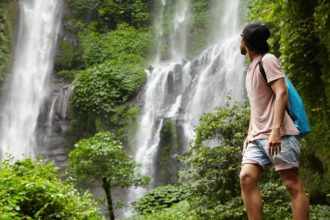 People, wildlife and adventure concept. Fashionable young adventurer with backpack contemplating wat